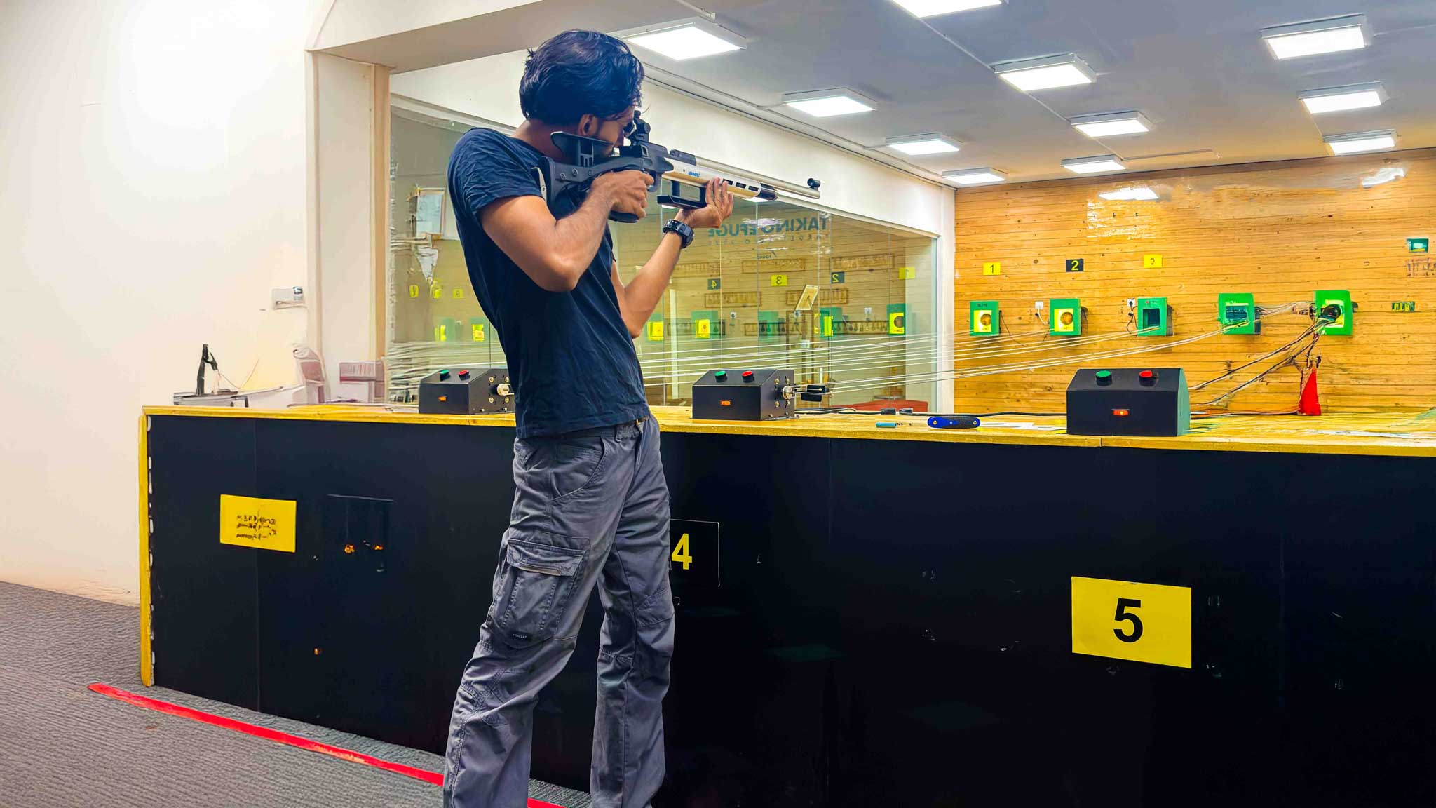A shooter taking aim with a rifle at targets in an indoor shooting gallery in Bengaluru.